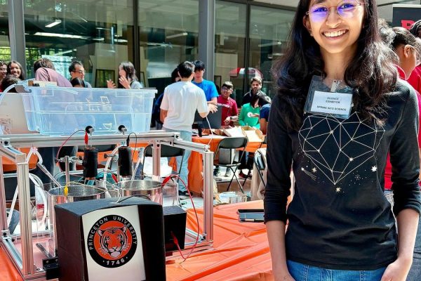 a teenage girl smiling as she stands in front of a table displaying her kelvin water dropper project
