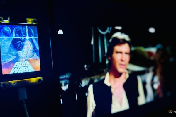cheap yellow display showing the star wars now showing poster with the movie playing blurred on the screen behind it