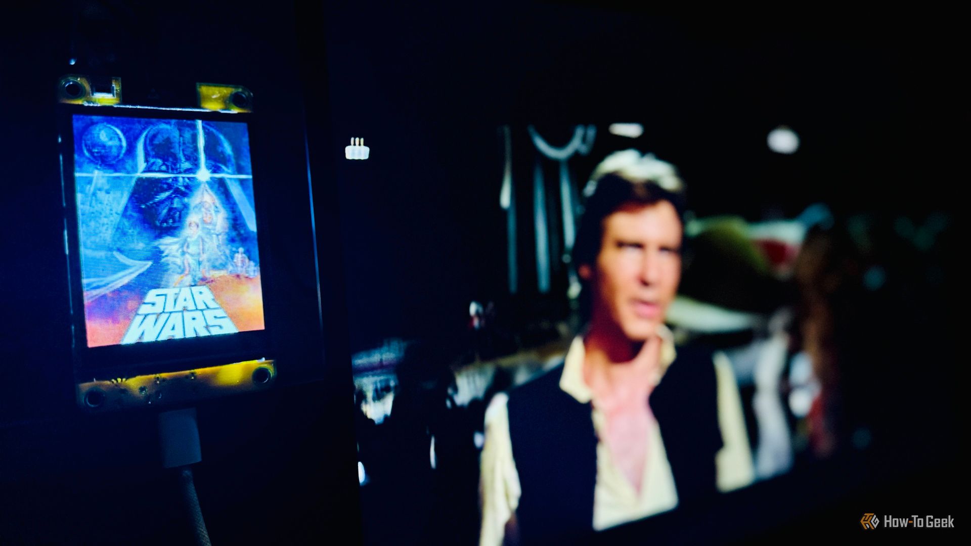 cheap yellow display showing the star wars now showing poster with the movie playing blurred on the screen behind it