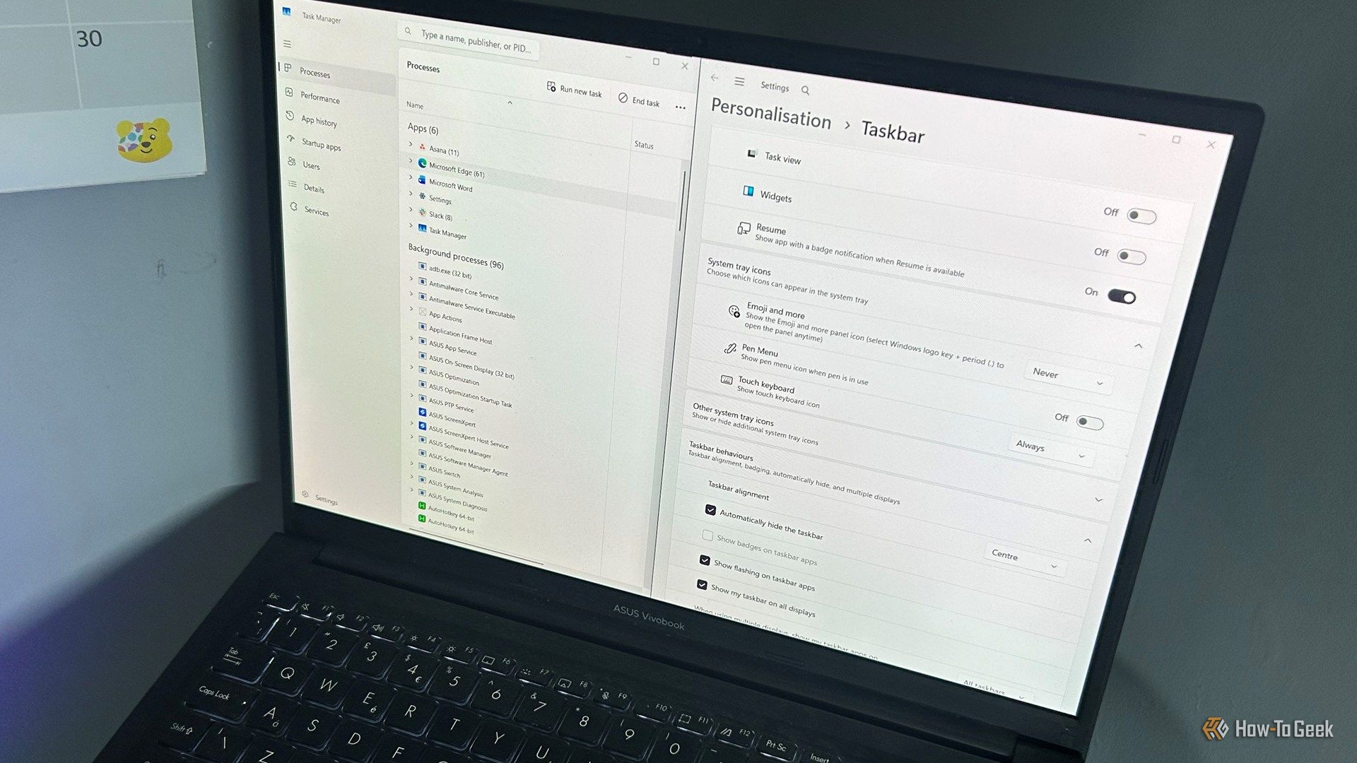 laptop photographed from above with windows 11 task manager and taskbar personalization open side by side